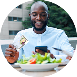 Junger Mann mit Ticket Restaurant® in der Hand isst einen Salat zur Mittagszeit
