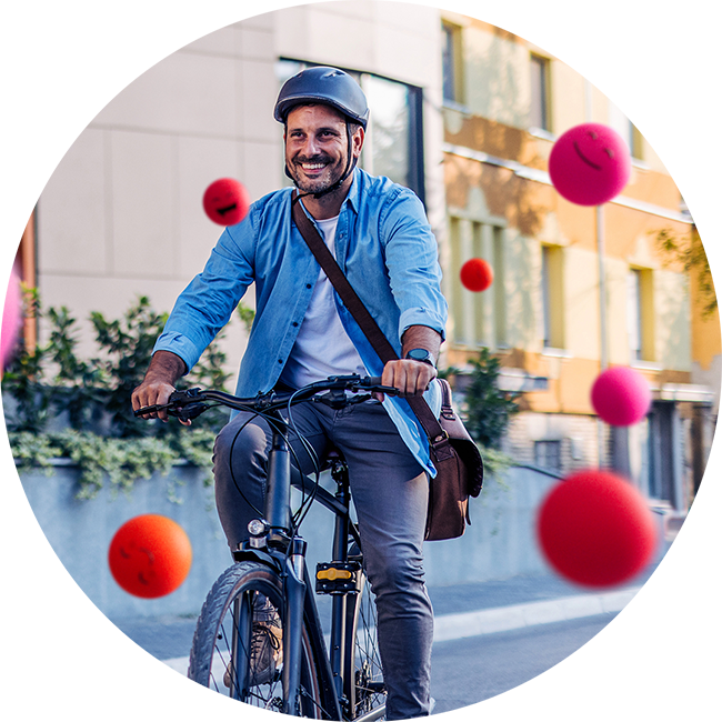 Mann fährt mit einem Fahrrad durch eine städtische Umgebung und trägt dabei einen Helm sowie eine Umhängetasche. Um die Szene herum schweben mehrere pinke und rote Kugeln mit fröhlichen Emoji‑Gesichtern.