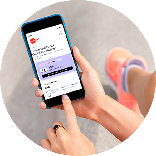 Person in Sportschuhen hält Smartphone mit der Ansicht „Urban Sports Club Gutschein einlösen“ in der Edenred-App. Betrachter schaut über die Schulter der Person